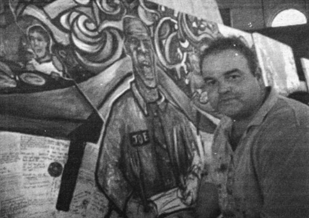 A photo of a man in front of a mural.