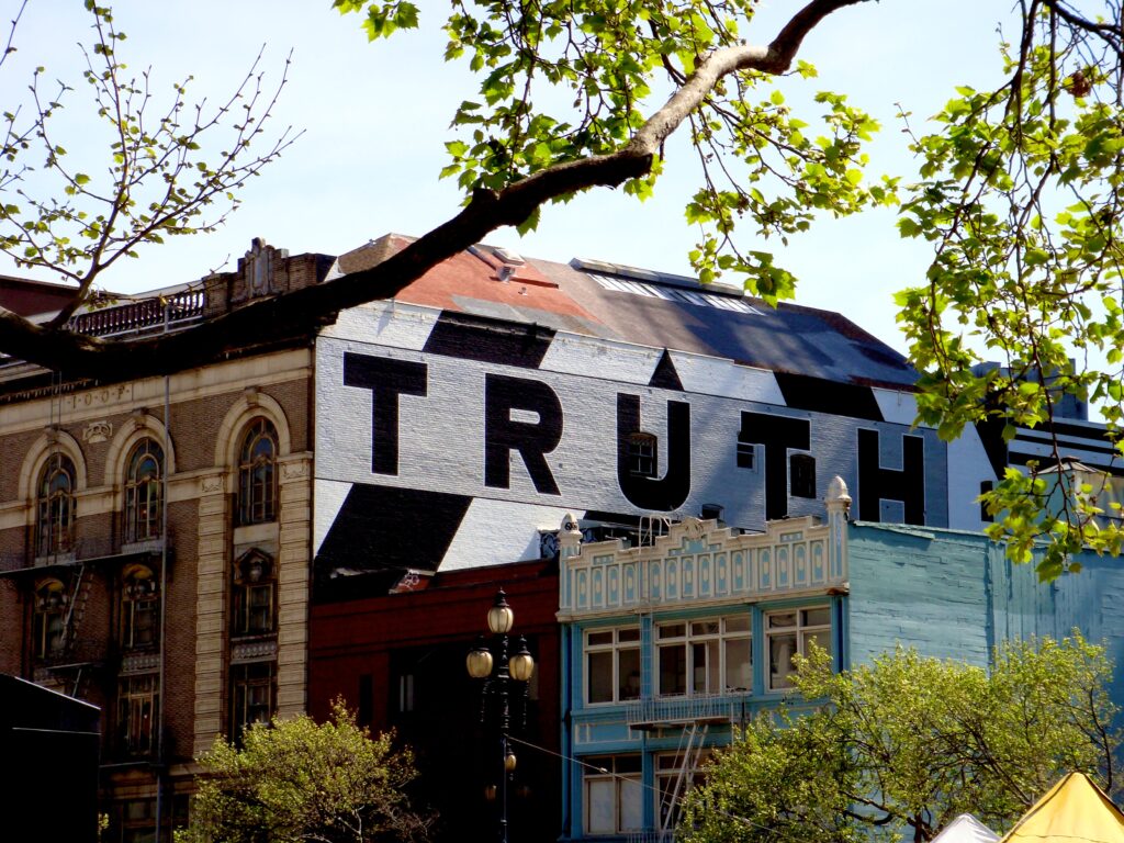 Photo displays the word truth written on a white building in black letters on a sunny day
