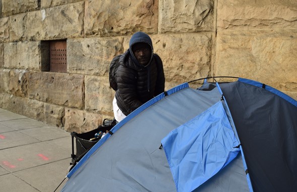 Photo of a man wearing a hoodie next to a tent.