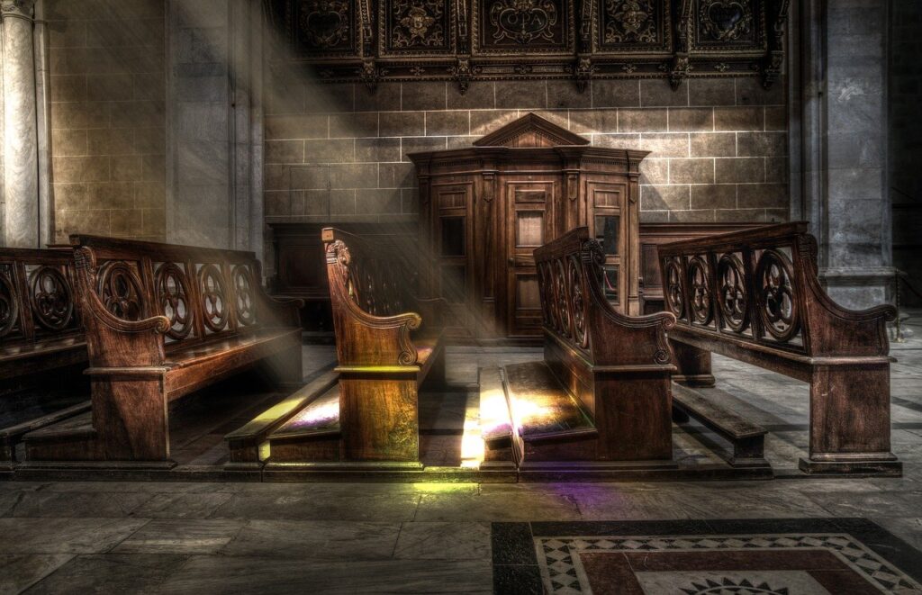 Image of empty church pews with a ray of light falling upon a kneeler.
