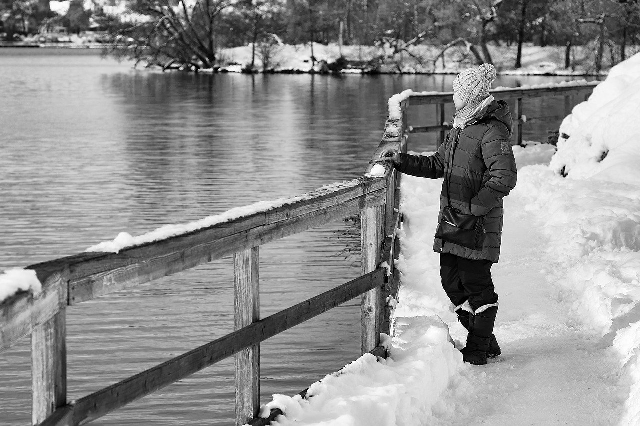 Image of a woman gazing at a river during winter; snow is on the ground and she wears winter clothing.