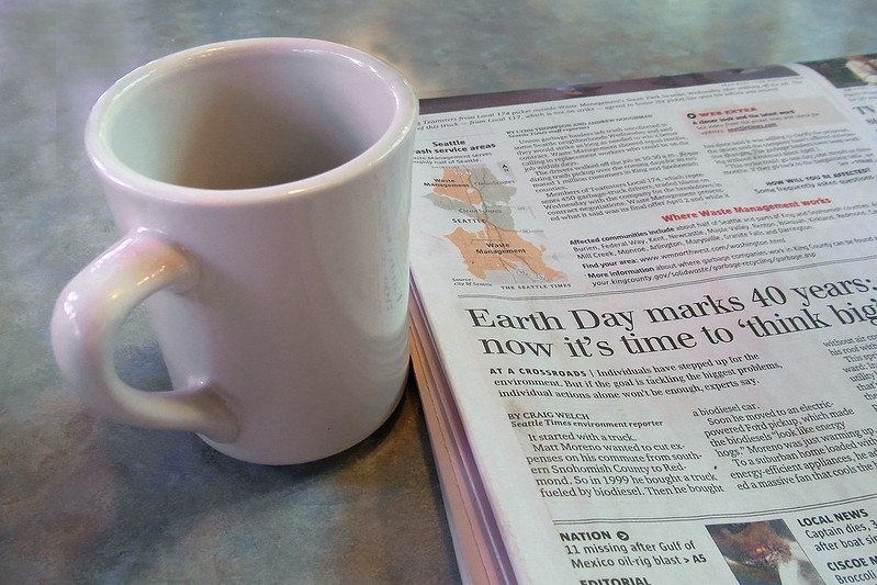 A phot of a newspaper and a cup of coffee sitting on a table.