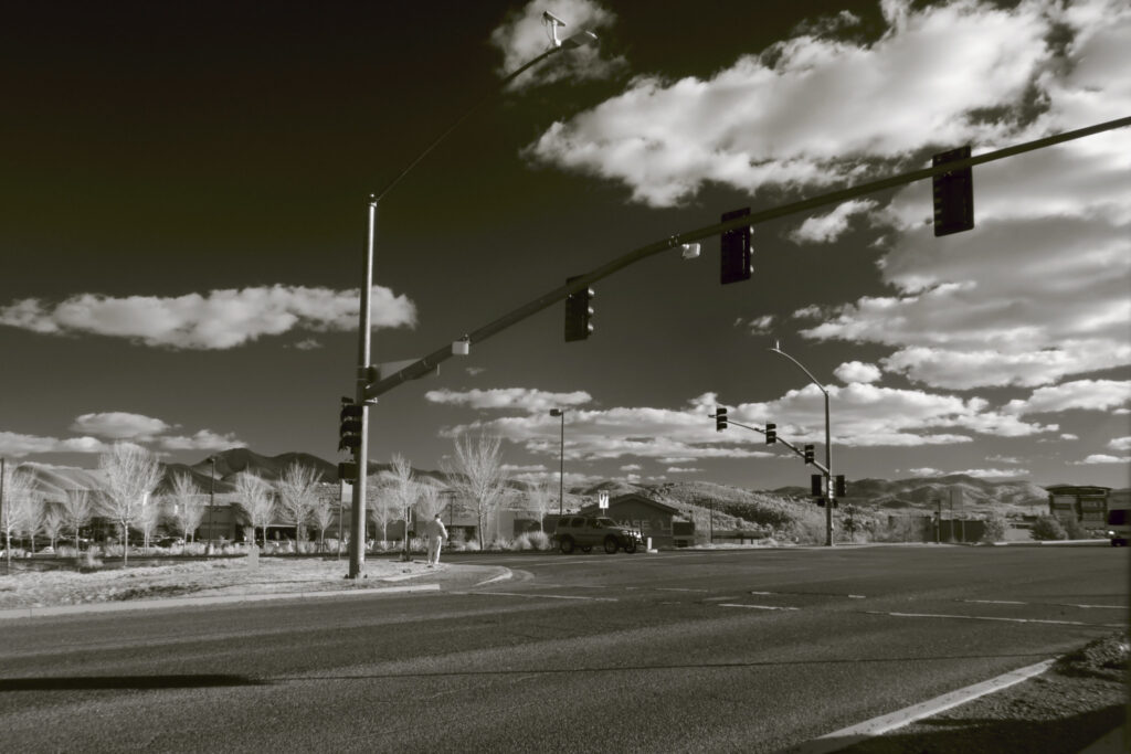 A black and white photo of a street with traffic lights, trees, and clouds.