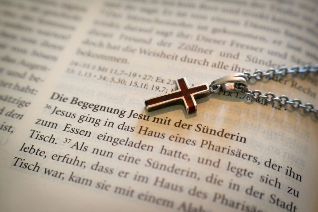 A photo of a chained crossed necklace placed on an open page of a Bible.