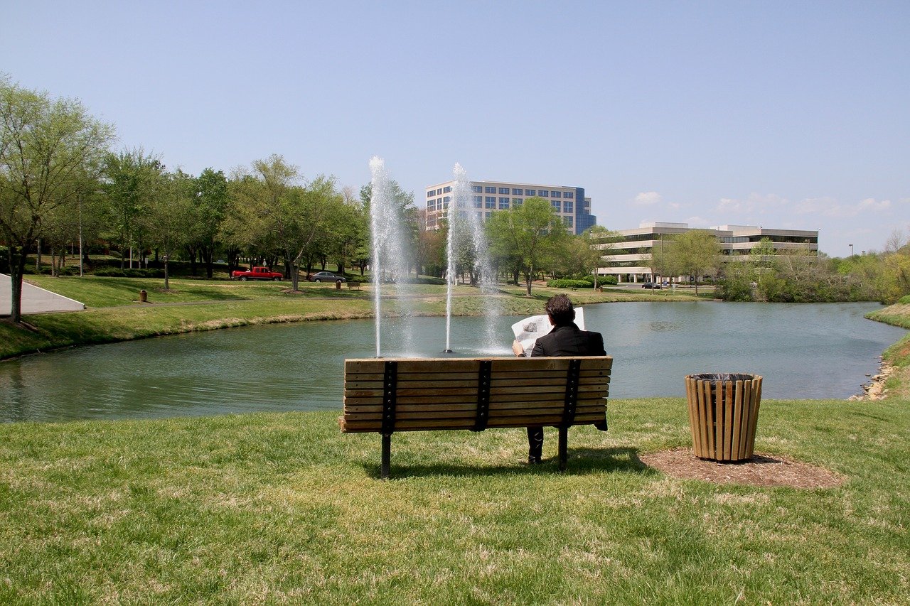 Photo of a man sitting at a park on a bench, reading a newspaper