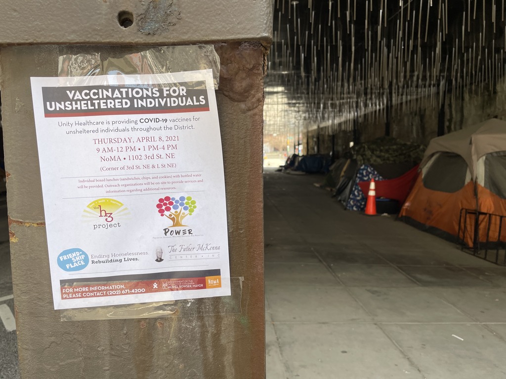 Image shows a flyer advertising vaccination clinics for people experiencing homelessness. There is a sidewalk with tents in the background.