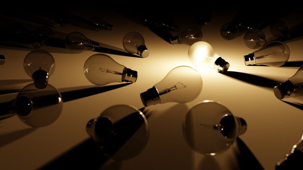 Image of a lit up light bulb surrounded by unlit light bulbs
