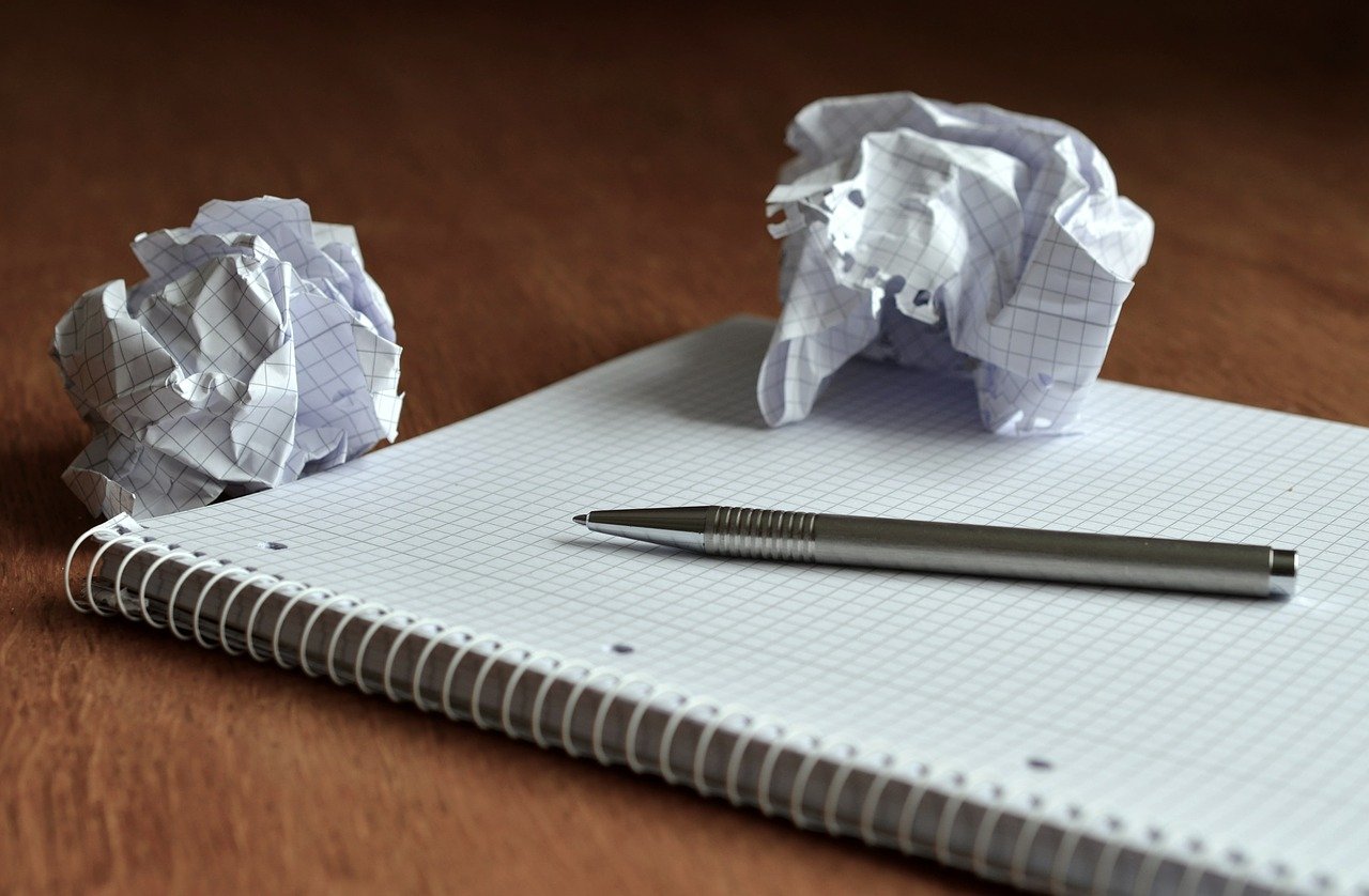 Image of a blank notebook, with a pen, and two crumpled pieces of paper on top of it.