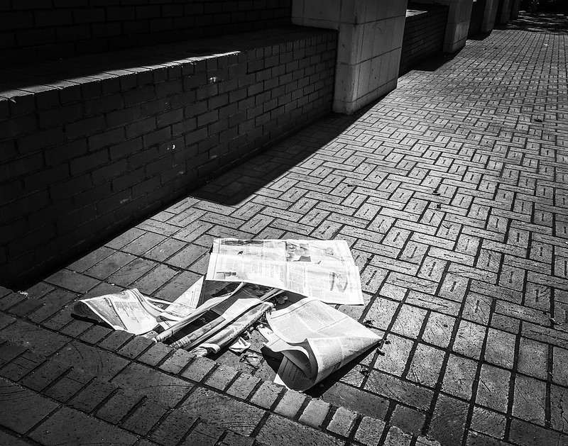 Photo of abandoned newspapers in an alley. The photo is in black and white.