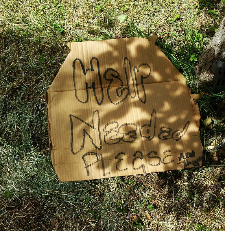 A photo of a discarded sign written on a piece of cardboard asking for help.