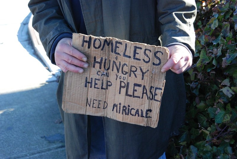 A homeless man holds a sign asking for help