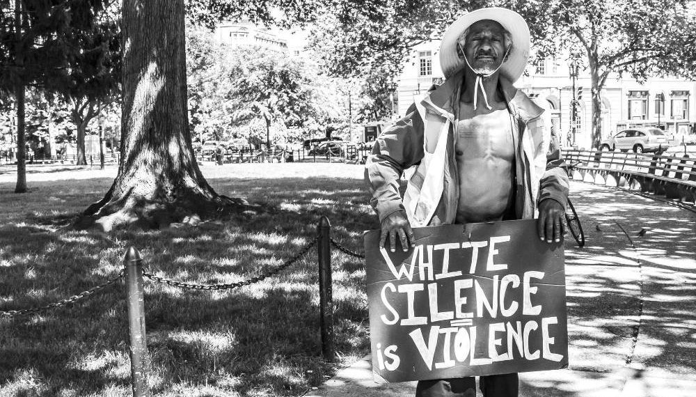 Photo of a man holding a sign that says "white silence is violence"