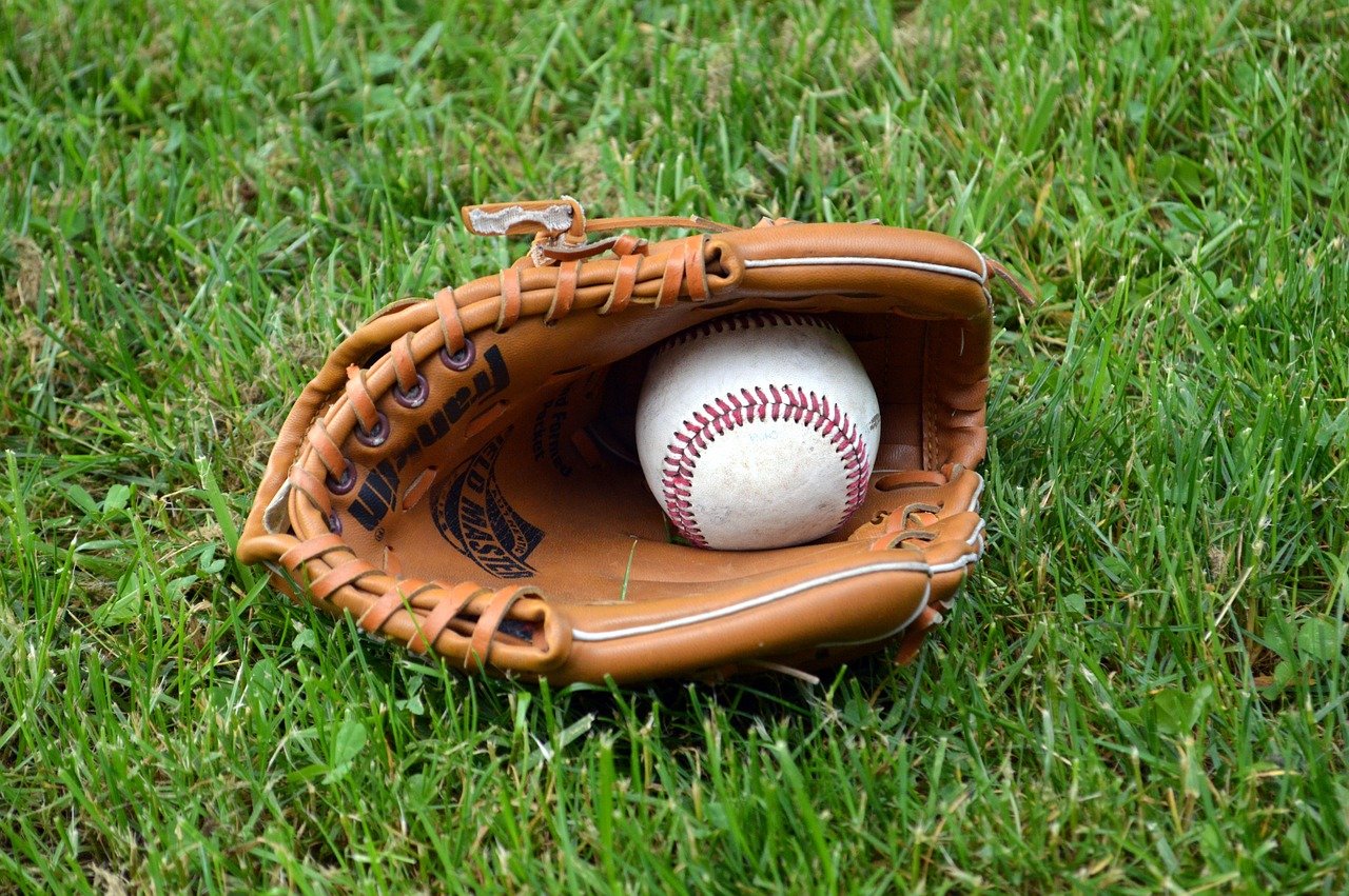 Photo of a baseball glove holding a baseball, and lying in the grass.
