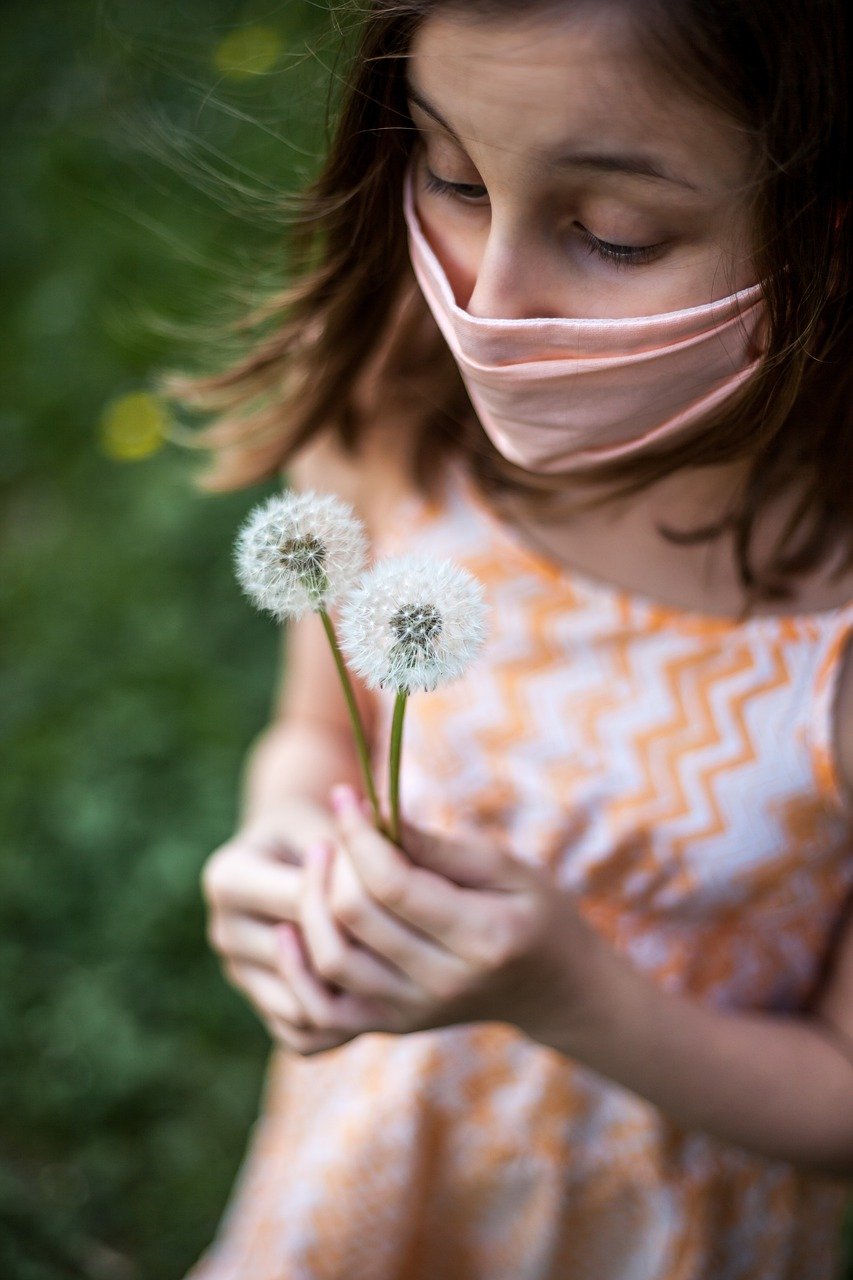 Photo of a young girl wearing a facemask holding dandelion seeds.