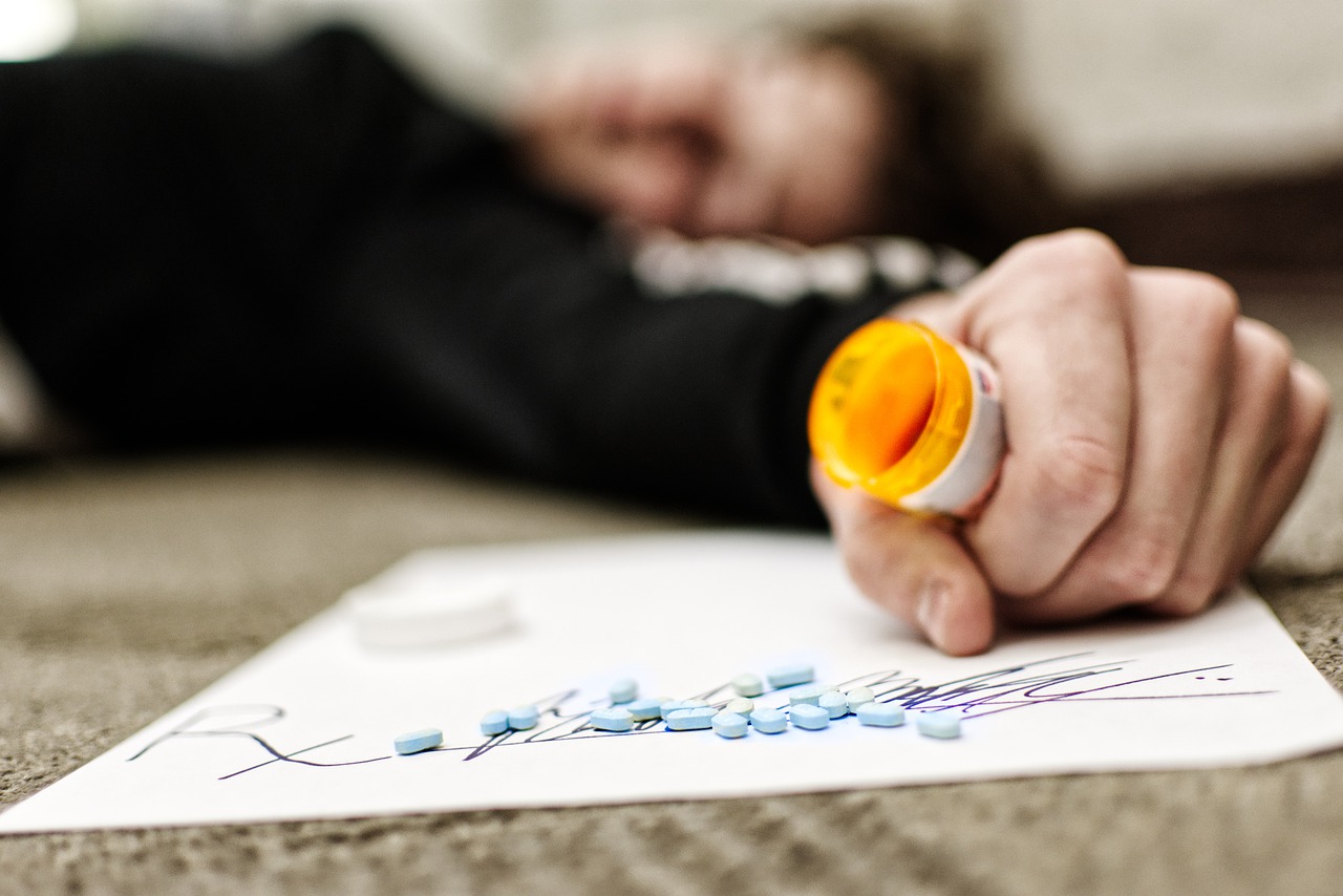A photo of a man holding an empty bill bottle with a cluster of pills laid on the ground.