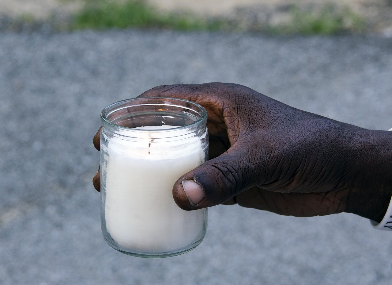 A hand holds a jar containing a lit candle.