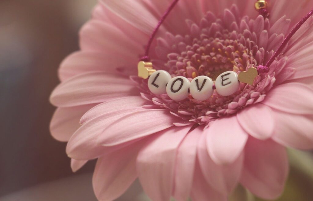 A photo of a bracelet that says "love" laying on top of a pink flower.