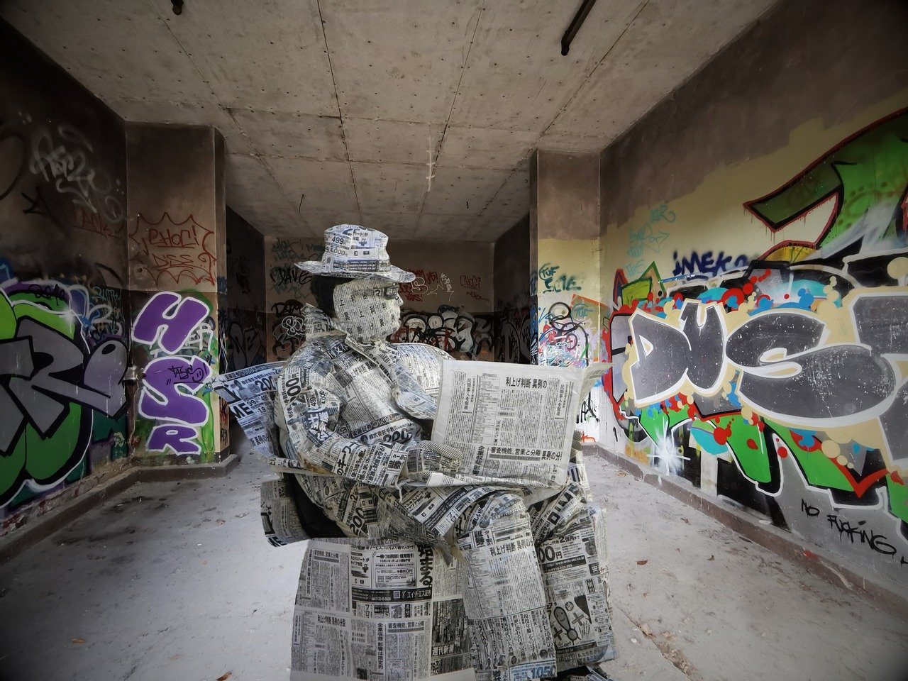 A man or statue covered in newpapers sits and reads a newspaper.