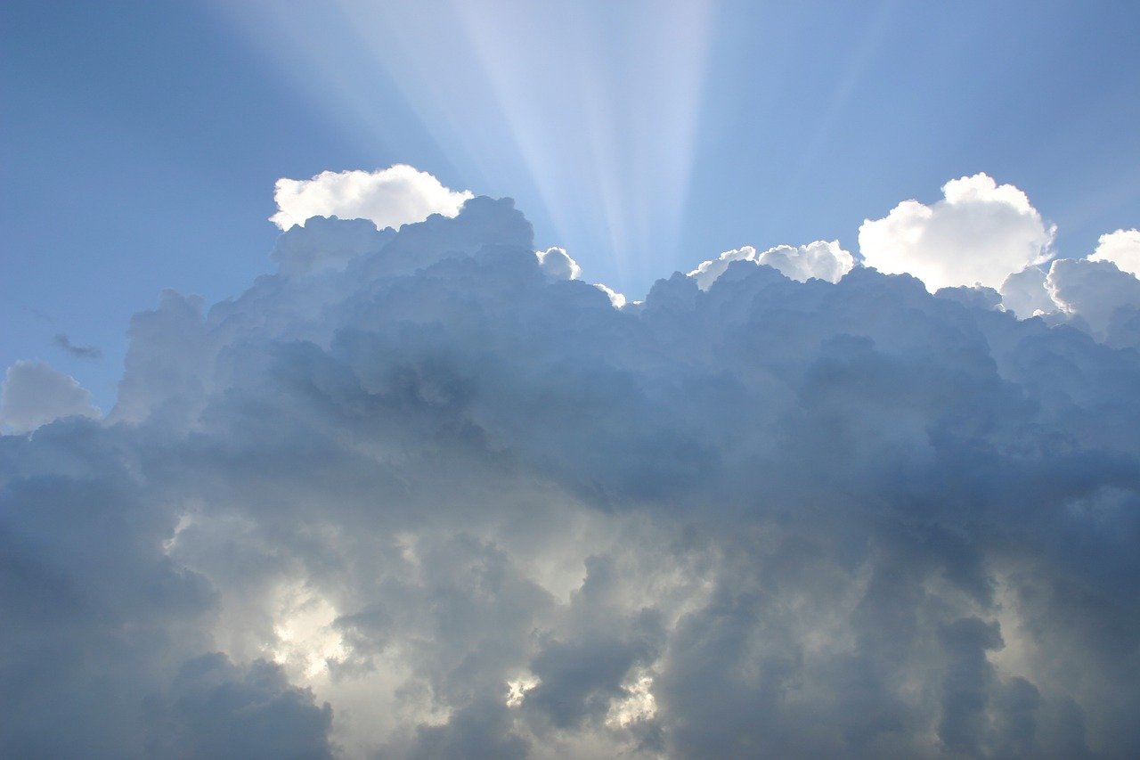 Photo of rays of light shining behind clouds in a bright blue sky