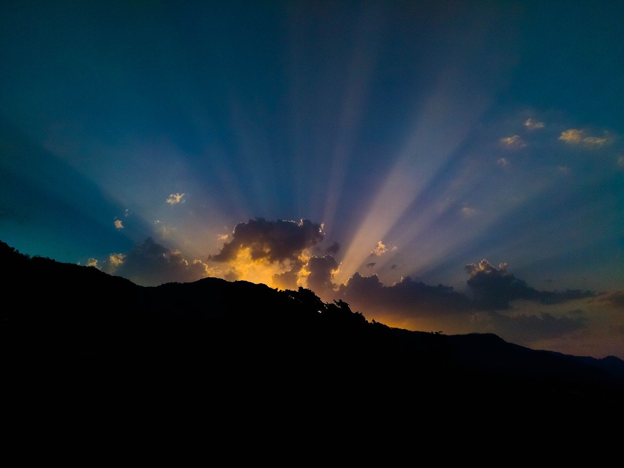 Photo of rays of light from a sun rise peaking out from behind a cloud.