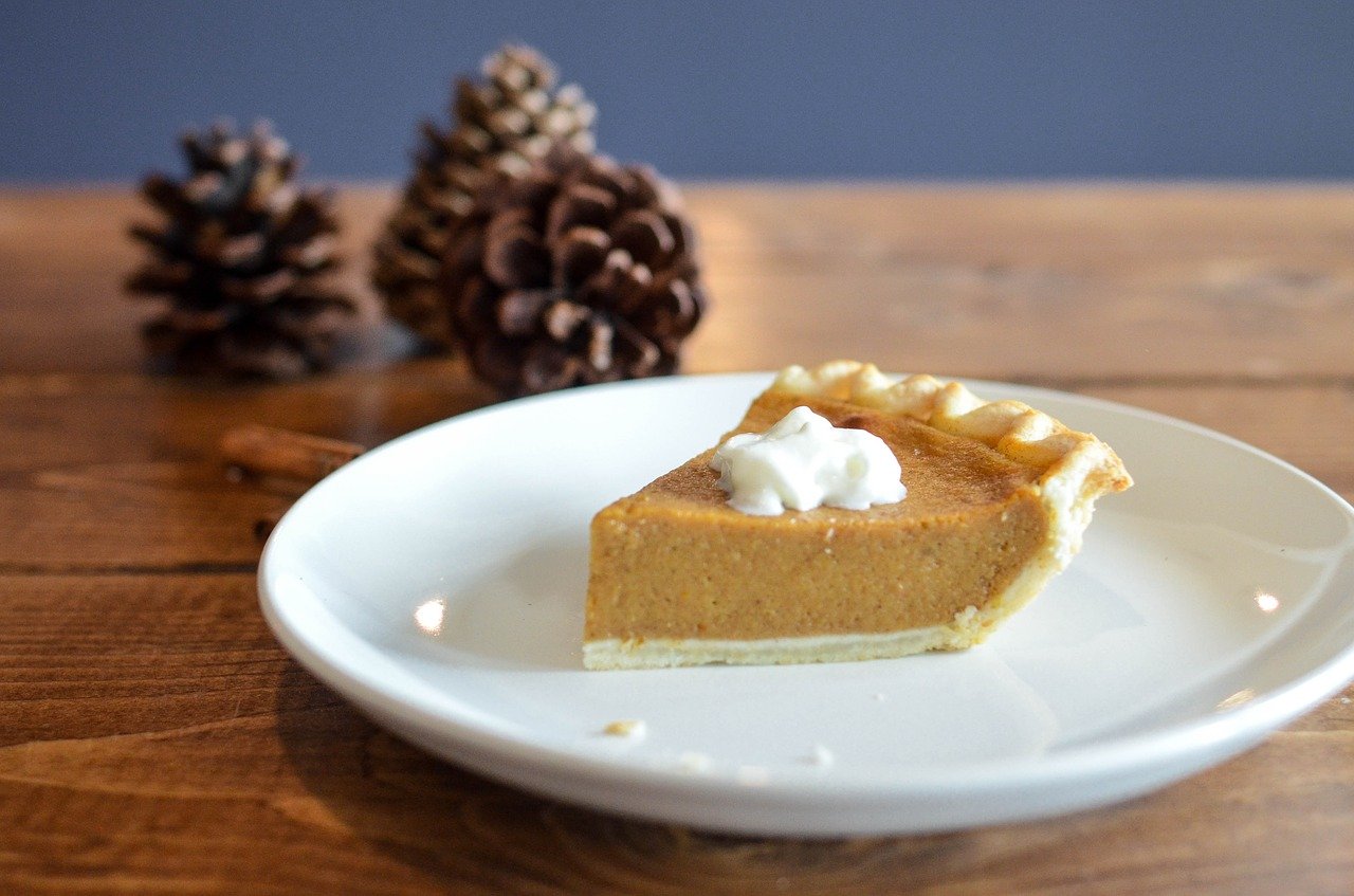 Photo of a slice of pumpkin pie with whipped topping sitting on a table.