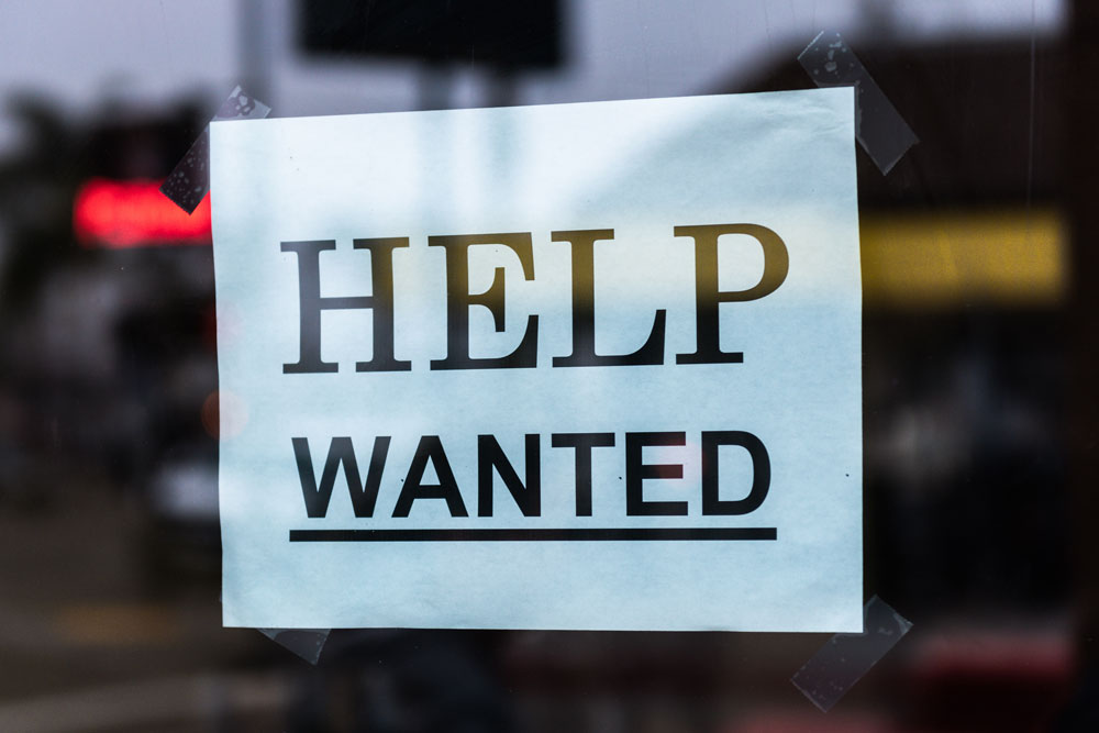 Photo of a "Help Wanted" sign posted in a window. Courtesy of Tim Mossholder on Unsplash.com