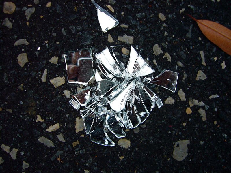 A reflection of a person taking a photo is visible in a broken mirror on the ground.