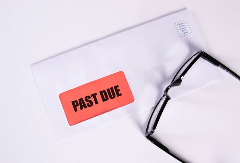 Stylized photo of a "Past Due" marked envelope with a pair of reading glasses sitting on top.