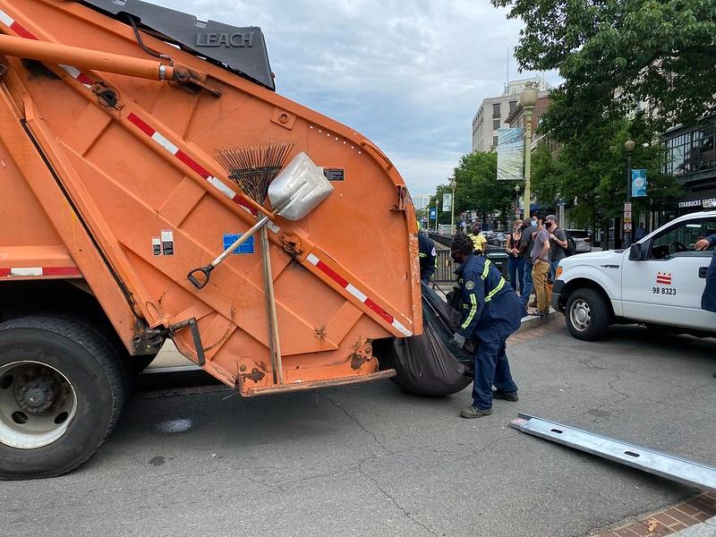 Photo of City employees loading a tent into the back of a garbage truck.
