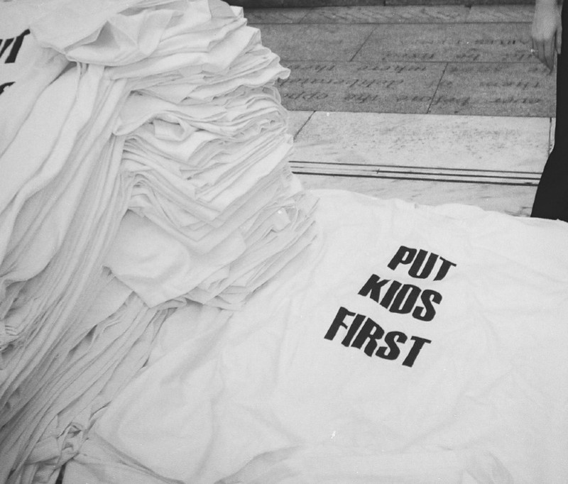 Piles of t-shirts that say "Put Kids First"