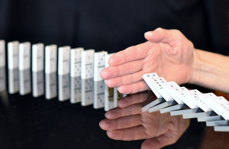Photo of a hand stopping a line of dominos from continuing to fall