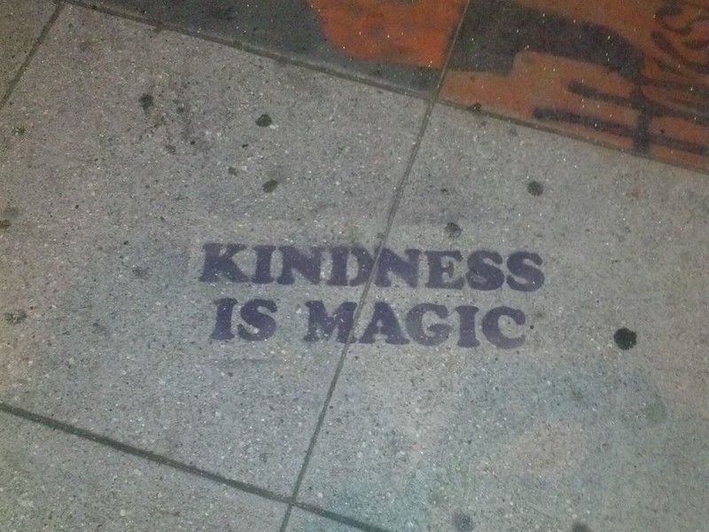 A photo of a sidewalk where "Kindness is Magic" is spray painted