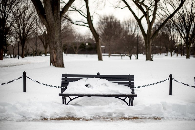 A park bench is shown nearly covered in snow