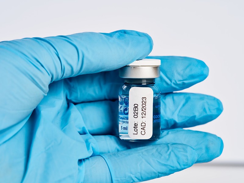Photo of a gloved hand holding a vial of COVID-19 vaccine