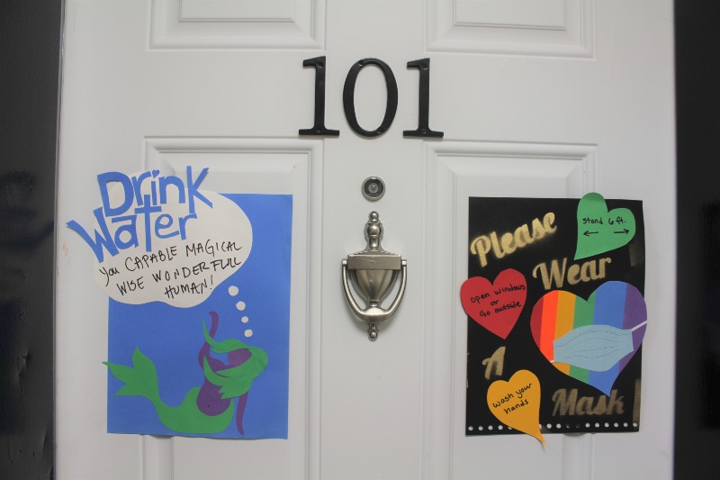 The apartment door is adorned with artwork encouraging healthy behavior and wearing a mask