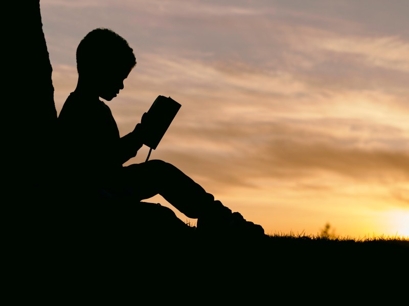 Photo of a shadow of a young boy reading a book