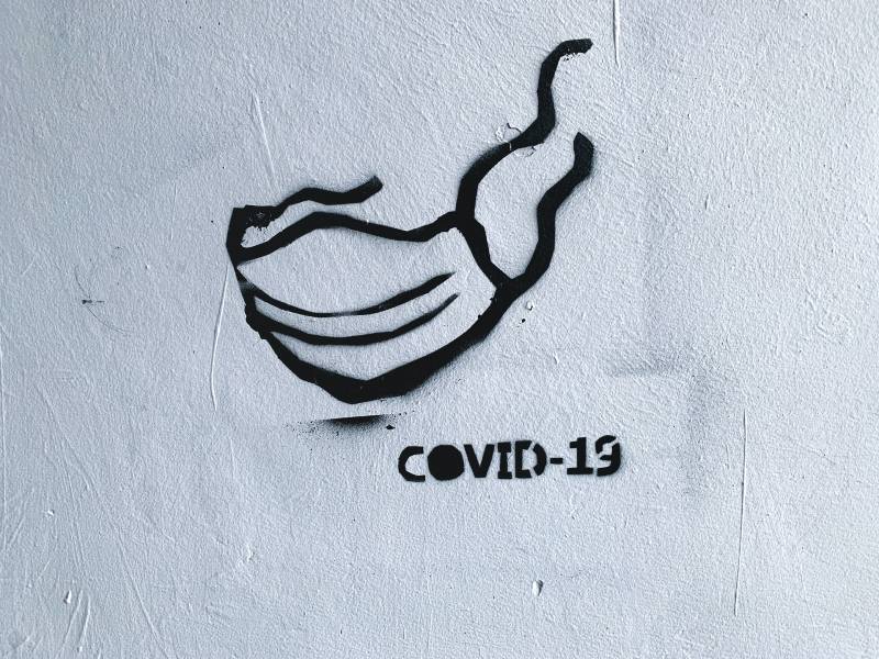Photo of graffiti on a wall that depicts a face mask and COVID-19