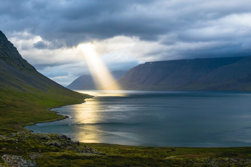 Photo of beams of sunlight breaking through dark clouds on a lake in a valley