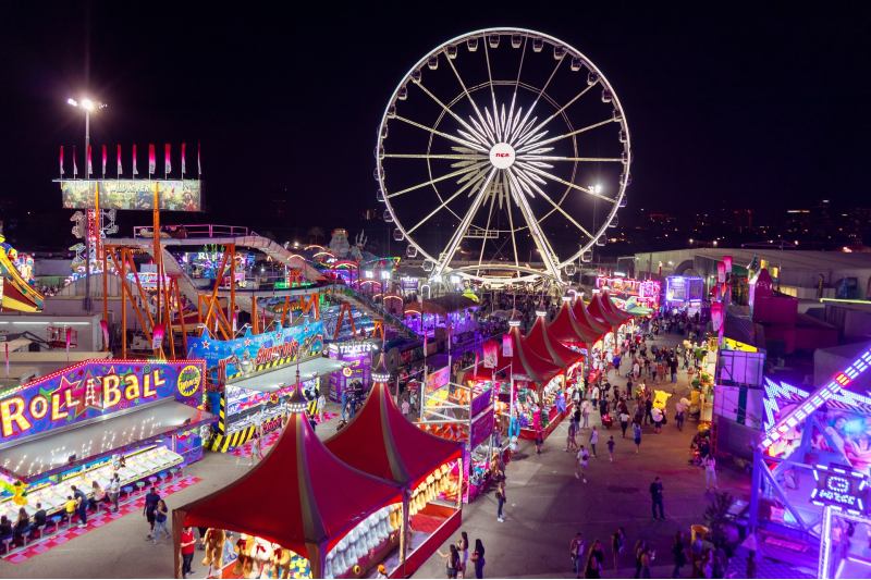 Photo of a carnival at night; shops, amusements, and rides are brightly lit