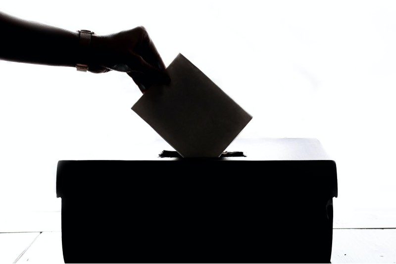 Photo of a shadowed hand depositing a ballot into a box