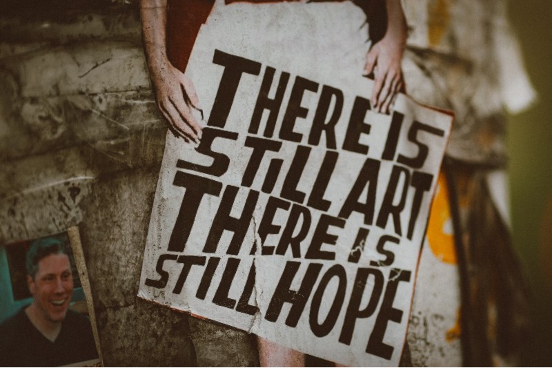 Photo of a person holding a sign that says "There is still art, there is still hope"