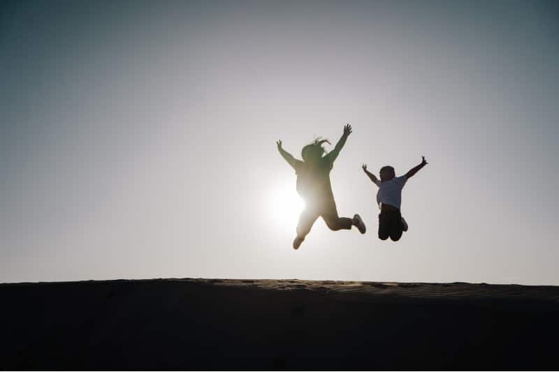 Photo of a mother and child jumping into the air in front of the shining sun