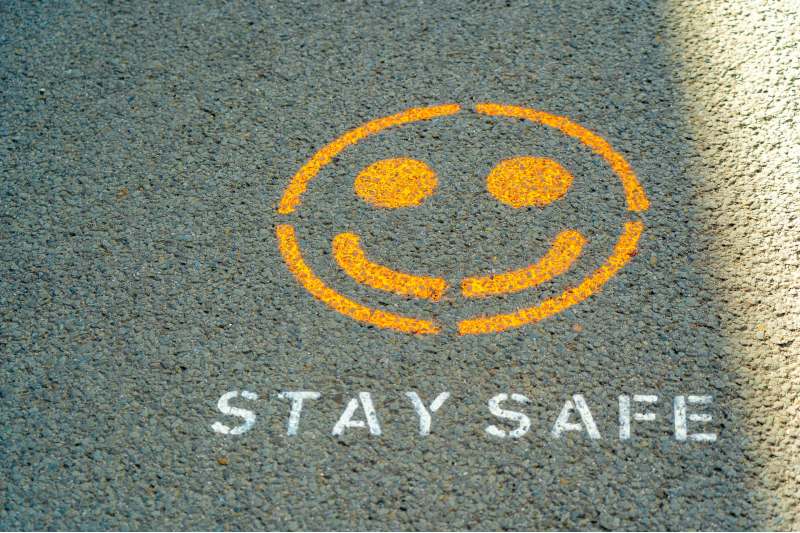 Photo of a smiley face painted on a sidewalk with the words "stay safe" underneath