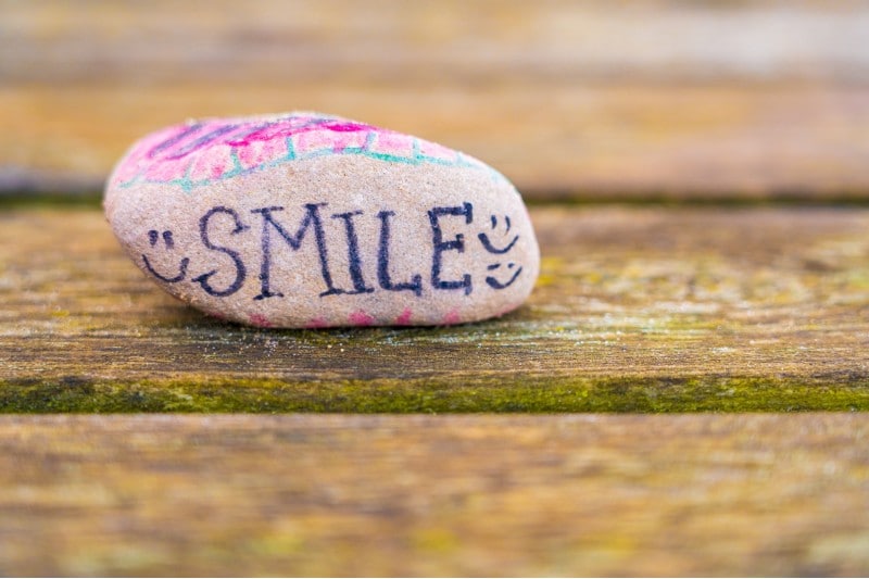 Photo of a painted rock that says "SMILE" with multiple happy faces