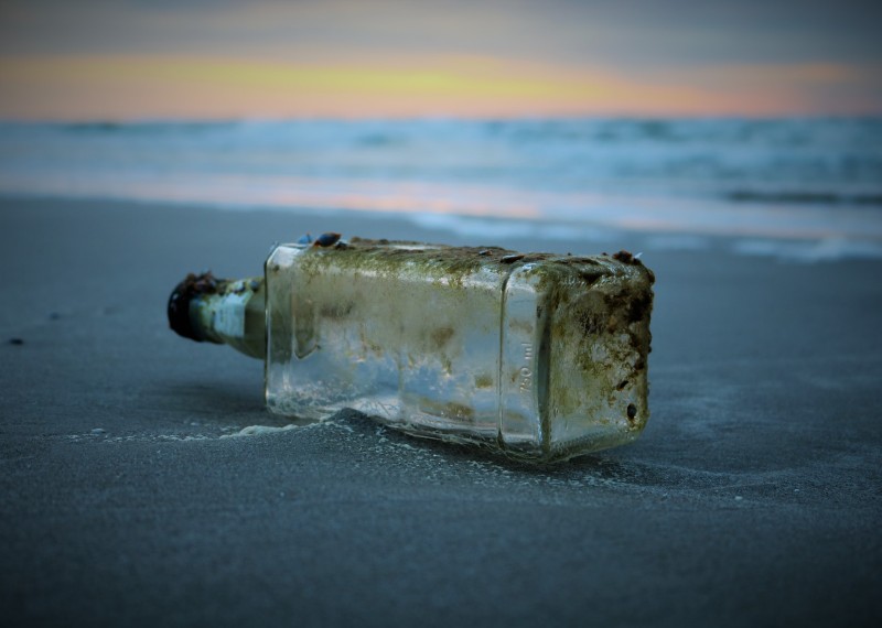Photo of an empty bottle laying on the beach.