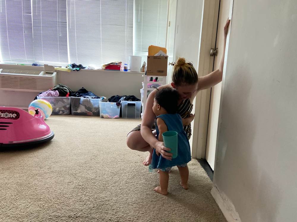 Photo of Jessica squatting down to hug her daughter in the middle of a mostly empty room.