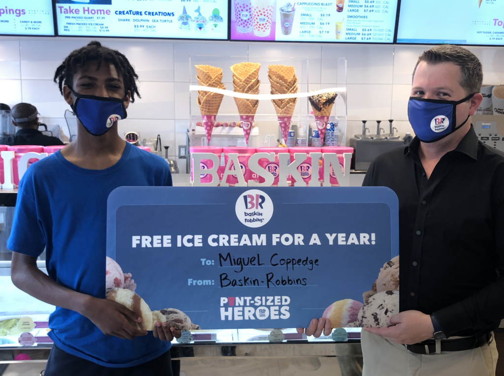 Photo of Miguel Coppedge and Baskin-Robbins employee holding up a check for free ice cream for a year.