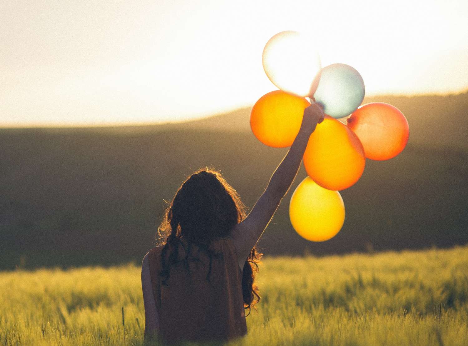 Photo of a woman holding balloons during the sunset.