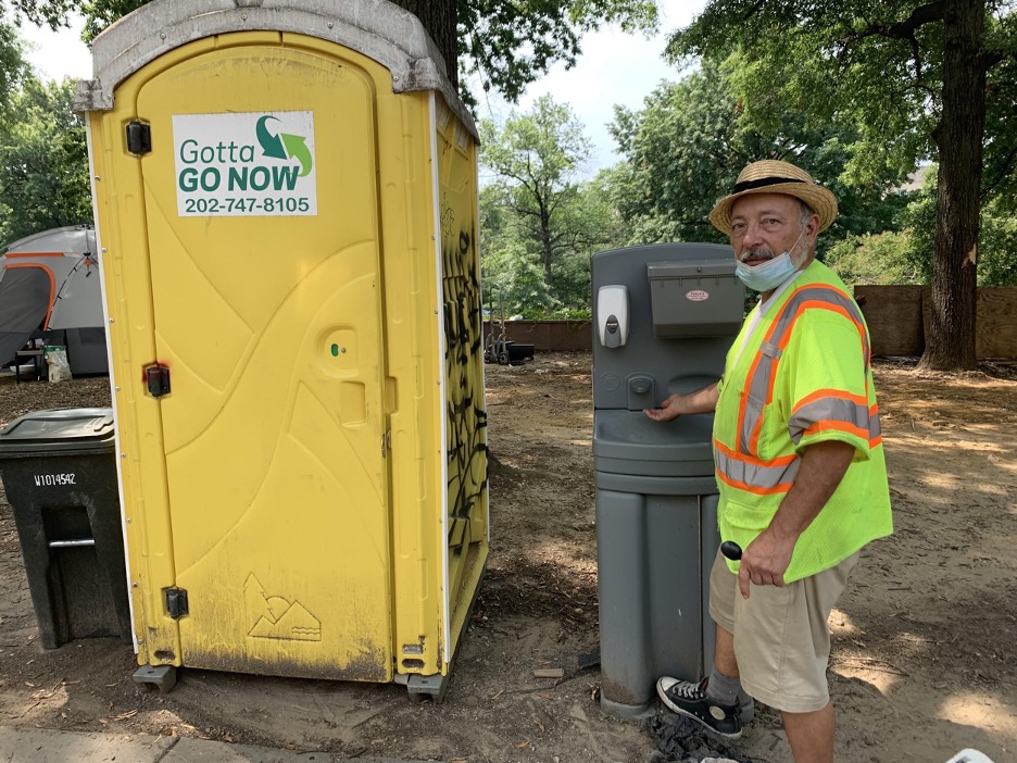 Photo of Daniel Rosas standing at a portable sink next to a portable toilet.