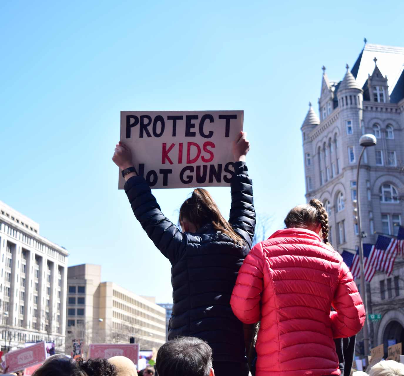 Photo of a woman holding up a "Protect kids not guns" sign at a protest.
